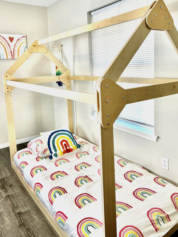Close view of a wooden house bed with colorful bedding beside a sunny window